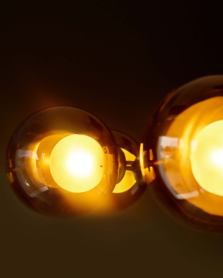 Close-up of three amber glass globe lights against a dark brown backdrop, exuding warm, inviting illumination.