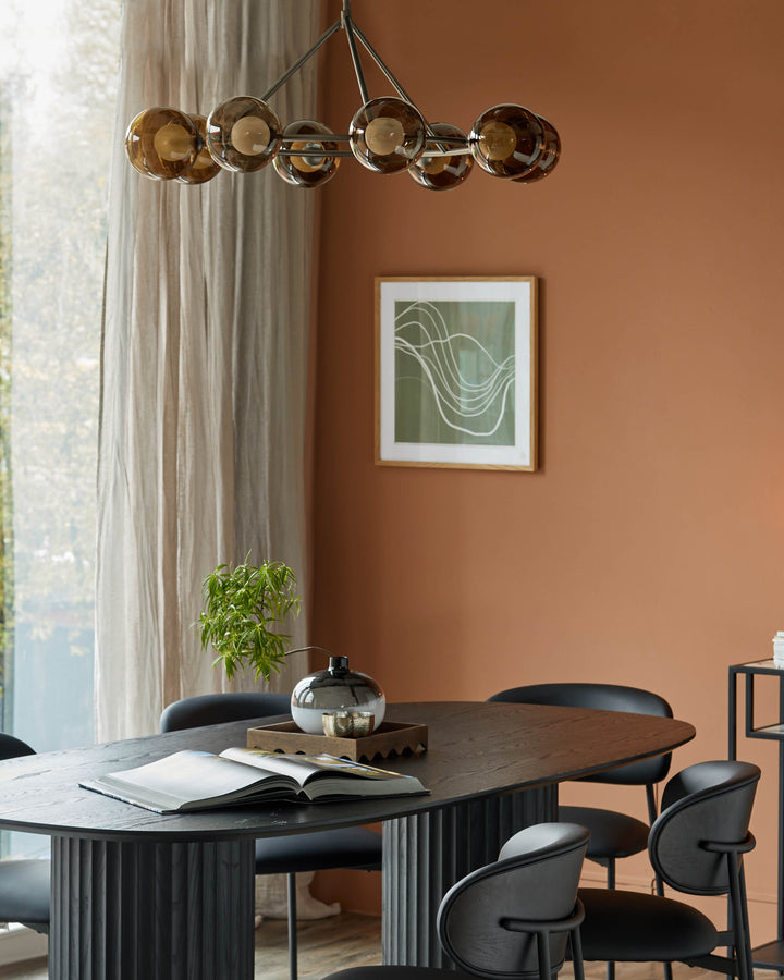 Dining set: a dark oval table with ridged base, surrounded by sleek black chairs. Modern lighting above.