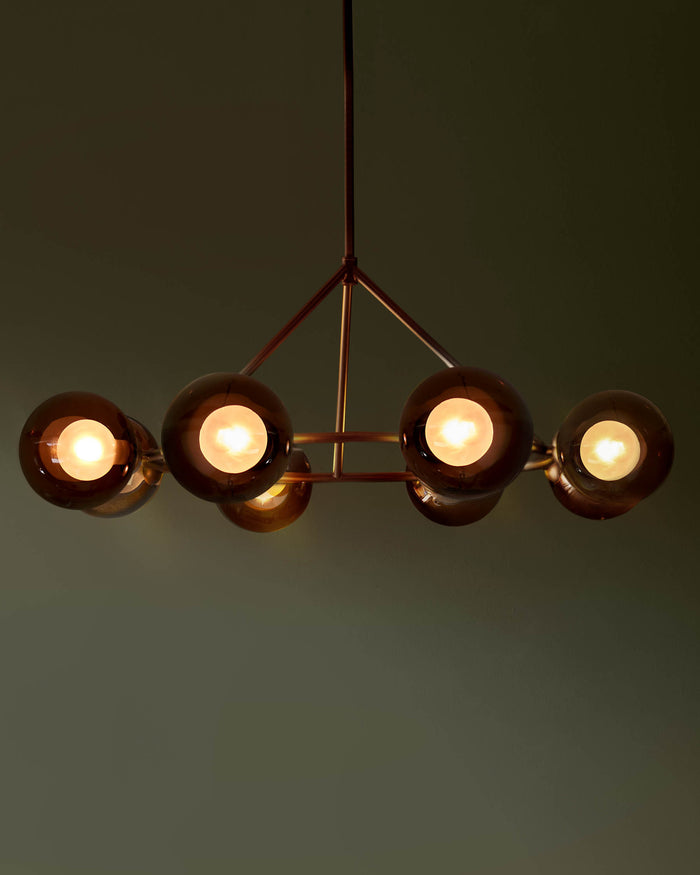 Modern light fixture with spherical glass shades, suspended from a metal frame against a dark backdrop.