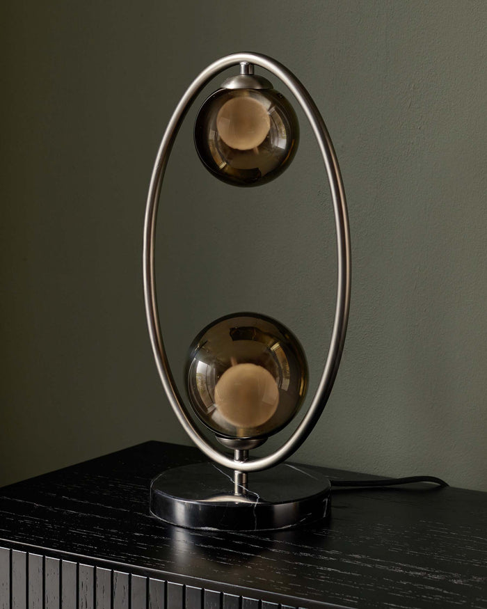 A modern lamp with two smoked-glass globes and a black marble base sits on a black wooden cabinet.