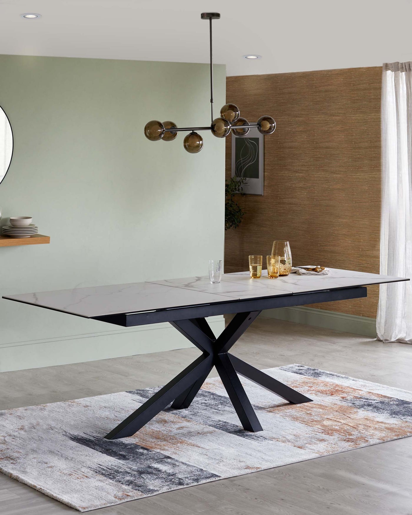 Modern rectangular dining table with a marble top and a bold, black cross-legged base, displayed on a textured area rug with abstract design in shades of white, grey, and burnt orange.