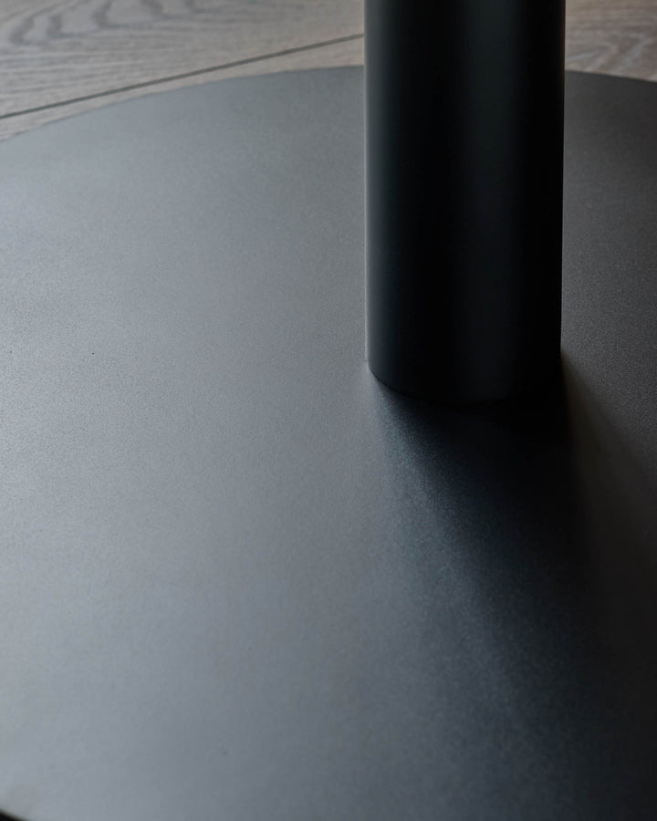 A close-up of a sleek, dark table base with a cylindrical leg, blending modern design with understated elegance.