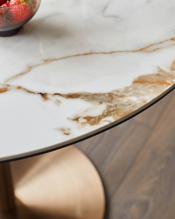 Close-up of a round marble-effect table with a metallic base and a bowl of strawberries on top, sitting on a wooden floor.