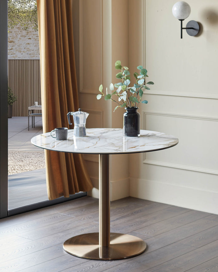 Marble-topped table with a brass-coloured base, styled with a coffee pot, mug and vase with sprigs.