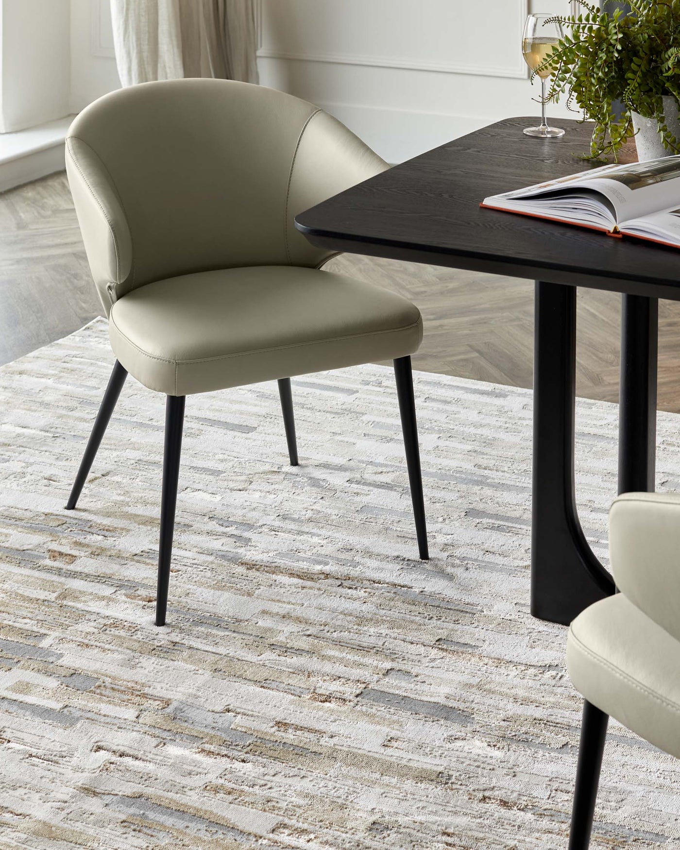 Contemporary-style furniture featuring a dark-stained wooden rectangular table with sleek black legs and a pair of elegant light grey upholstered dining chairs with a curved backrest and black tapered legs, set on a textured off-white area rug.