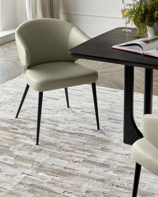 A modern dining set featuring a black wood table and stylish chairs with a muted green leather finish and black legs.