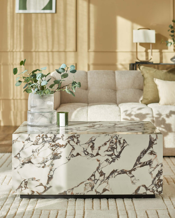 A stylish living room featuring a marble coffee table, sofa, and glass vase with eucalyptus.