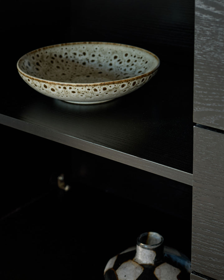 Russo sideboard in Calacatta white with dark wood shelving displaying a speckled ceramic bowl and decorative objects.