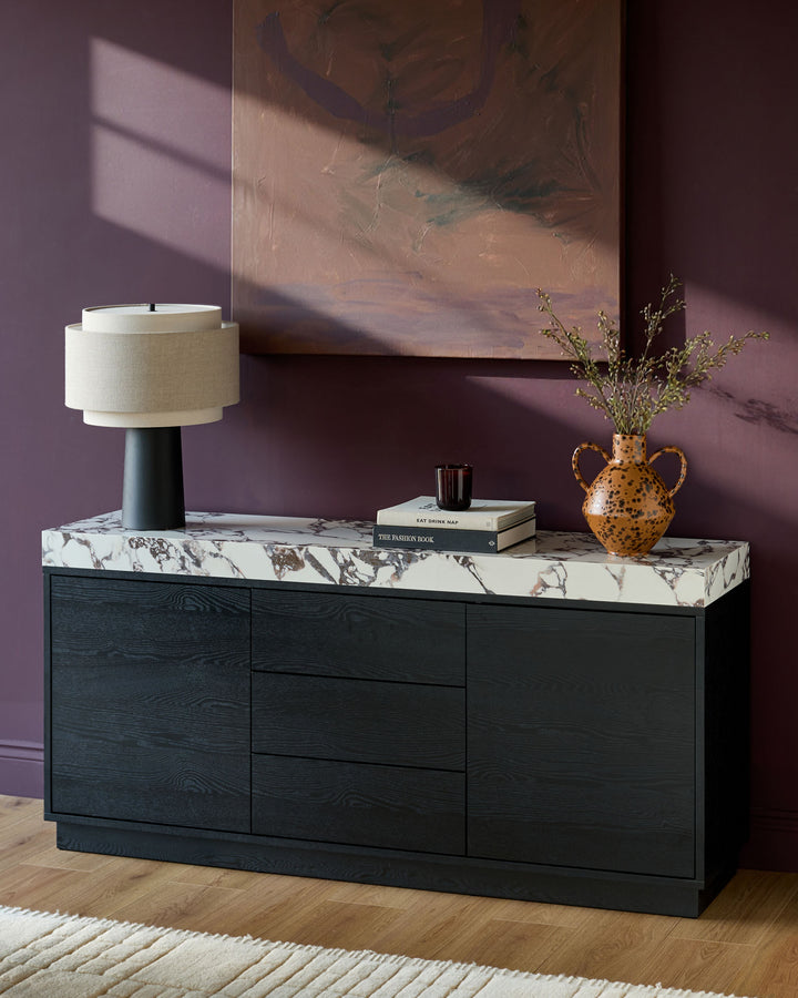 Russo sideboard in black wood with Calacatta white marble top, styled with lamp, books, and gold vase.