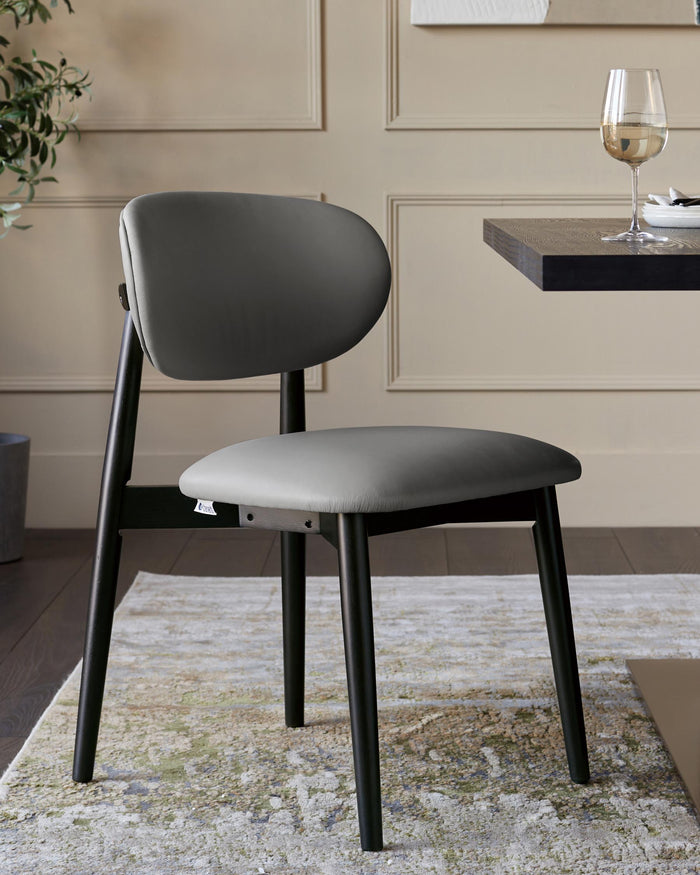 A grey upholstered dining chair with black legs sits on a patterned rug next to a table with wine and plates.