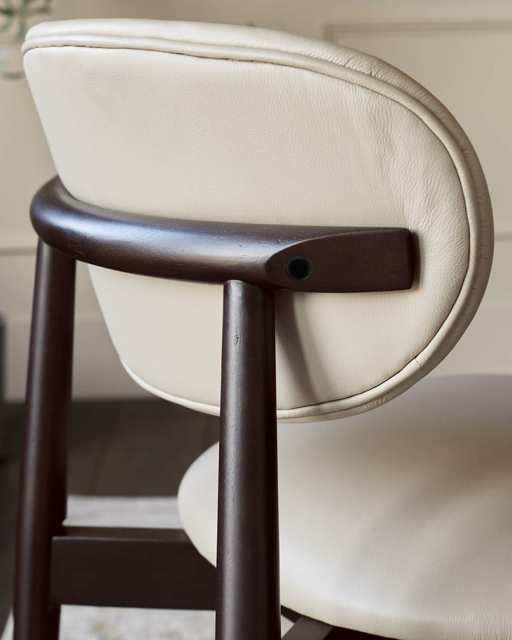 A close-up of a light-coloured leather chair with a curved wooden back support and frame.