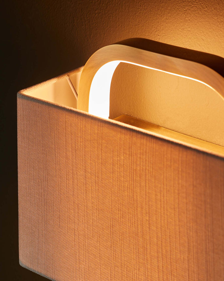 A stylish, lit wall light with a rectangular fabric shade and a curved wooden arm, adding a warm glow to any room.