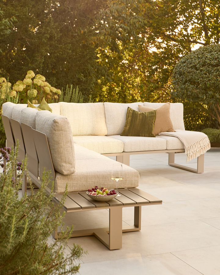 Savannah garden extra-large corner sofa in natural with wooden base, styled with cushions in a lush garden setting.
