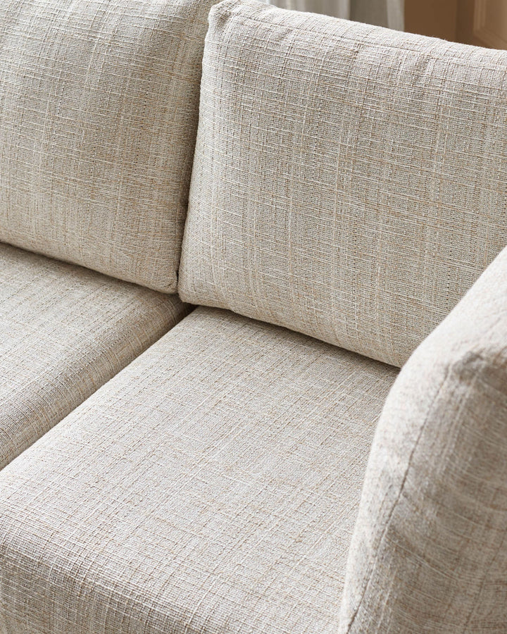 Beige linen upholstered corner bench with cushioned seat and back pillows, close-up detail view.