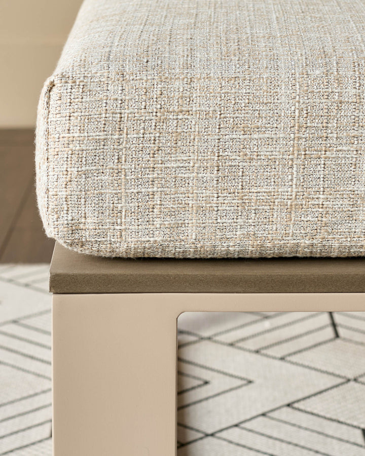 Natural linen bench with textured fabric seat, wooden base, and geometric patterned rug underneath, angled side view.