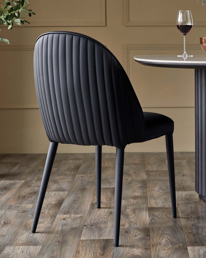 A modern black dining chair with a cushioned, vertically-stitched back. Part of a dining table and a glass of wine are visible.