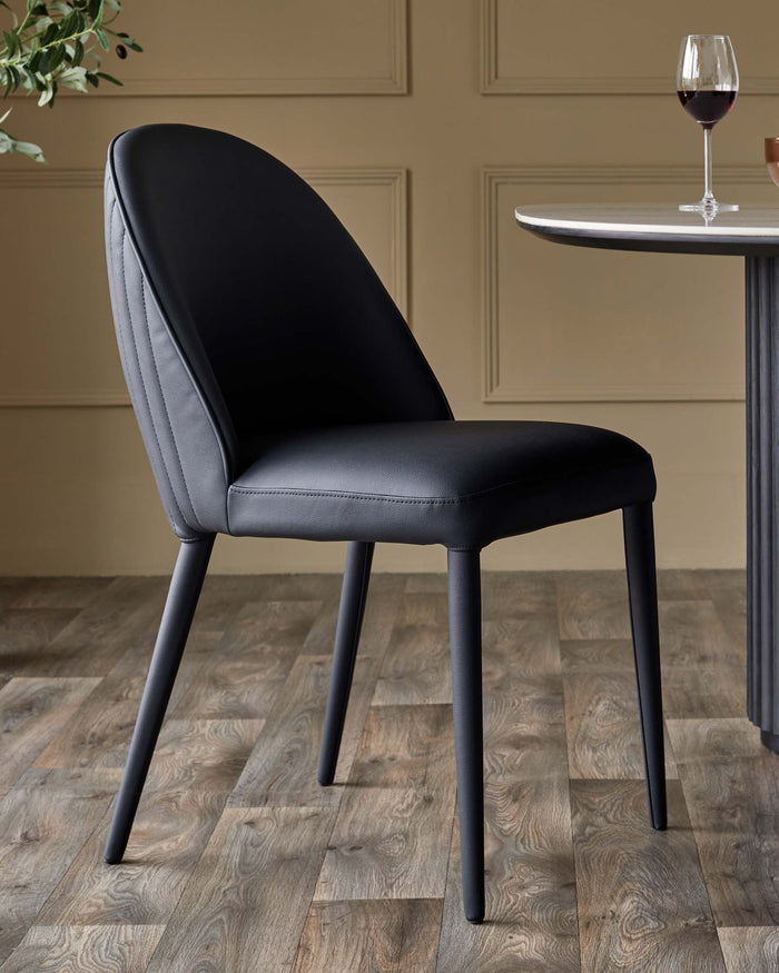 Stylish black dining chair and part of a dining table with a glass of red wine on top, sat on a wood-effect floor.