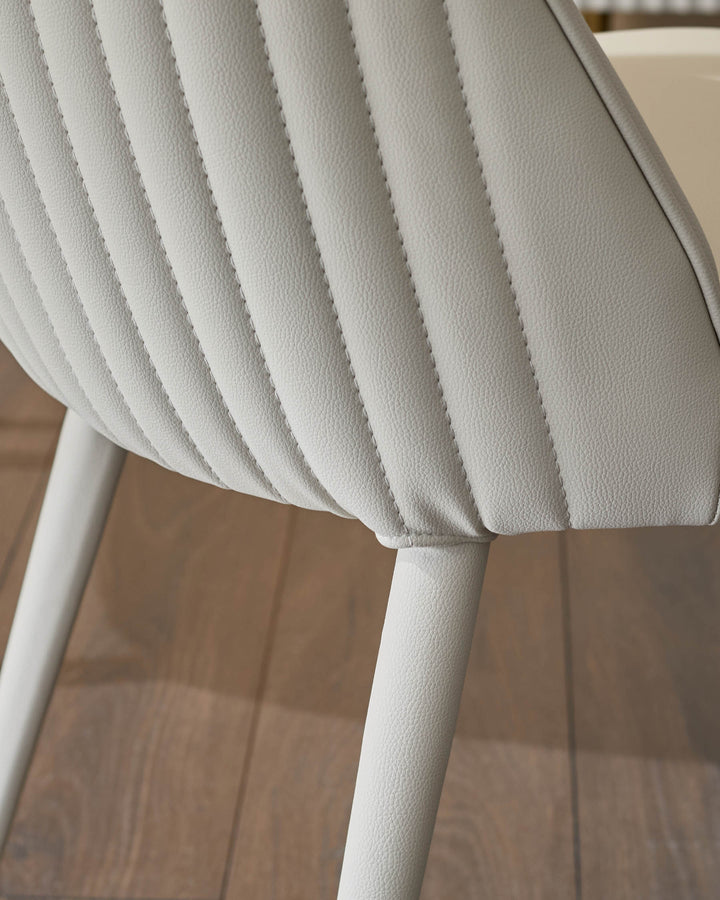 Close-up of light grey faux leather dining chair showing quilted backrest detail and white leg.