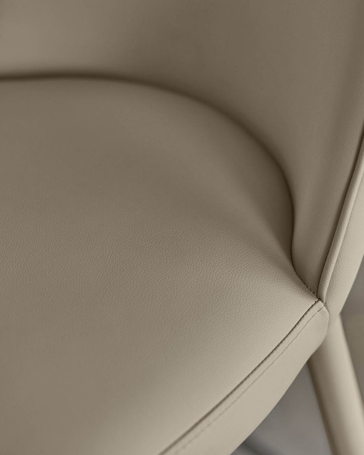 Close-up of a stylish, upholstered chair in a neutral, creamy colour. Features sleek lines and detailed stitching.