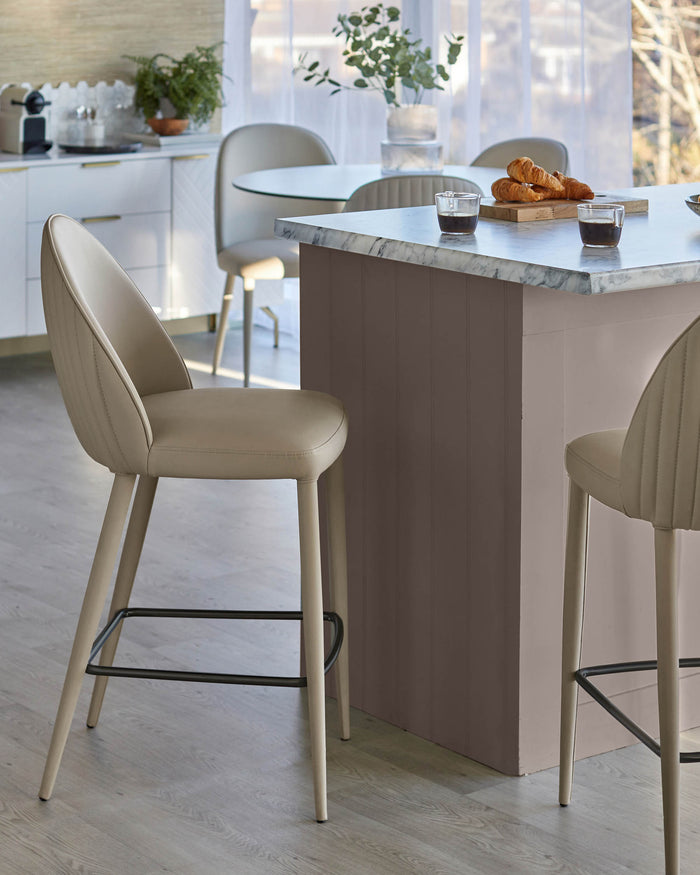 Stylish kitchen with breakfast bar and beige bar stools. Seating area with table and chairs in the background.