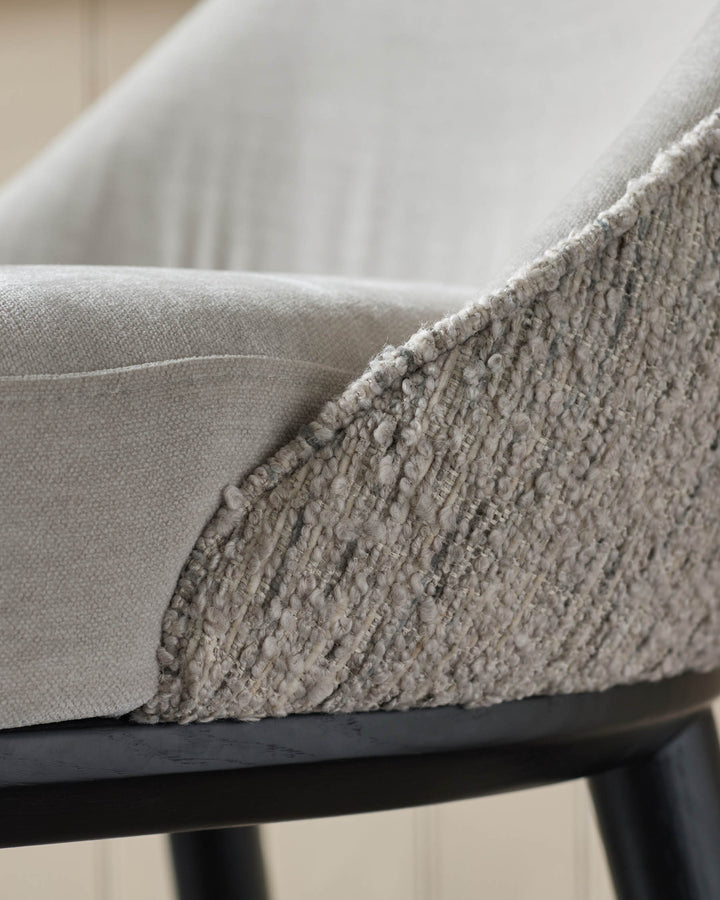 Close-up of a stylish chair featuring a textured, light-grey fabric and sleek black legs.
