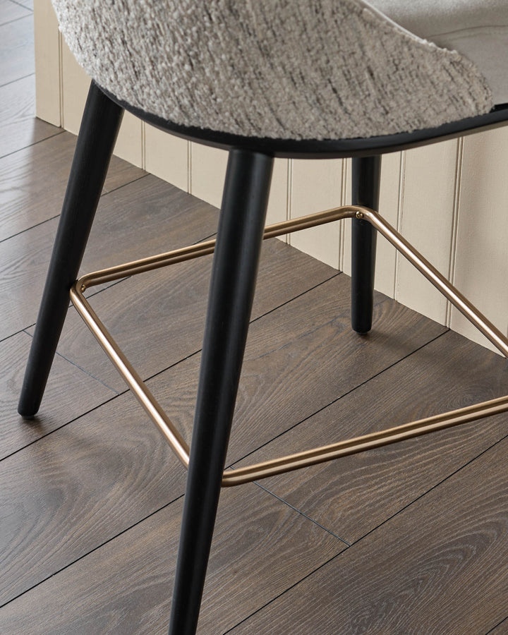 Close-up of a modern chair with black legs and a gold footrest, showcasing its texture and design details.