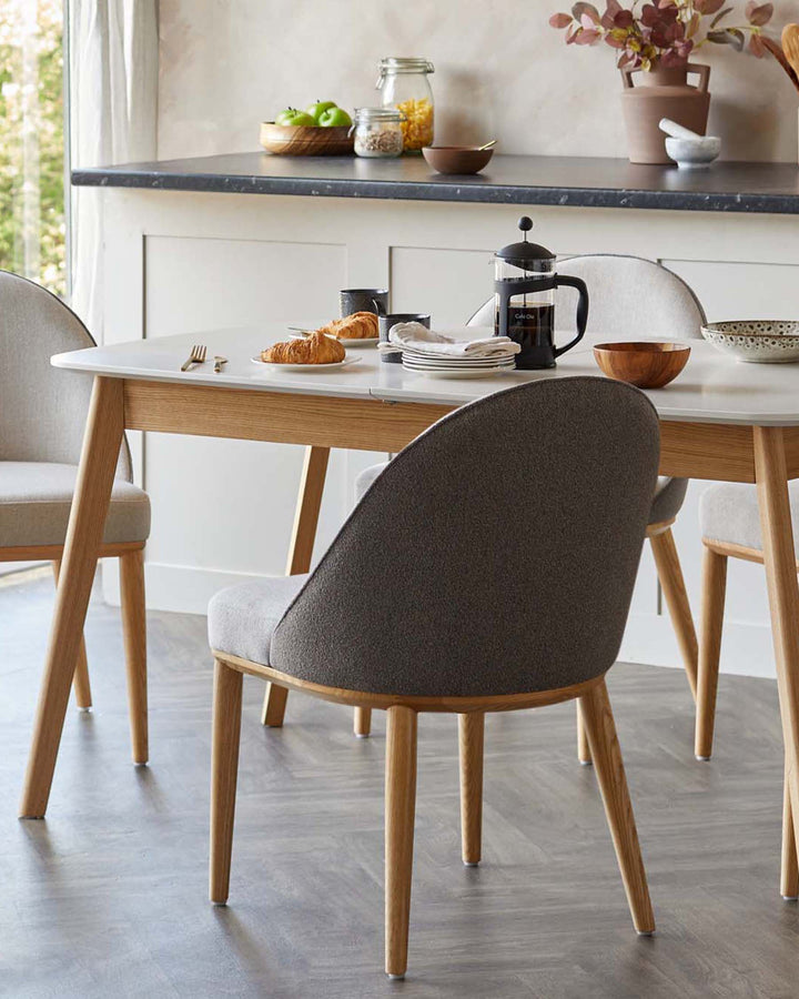 Dining table with a white top and light wooden legs, surrounded by grey upholstered chairs with matching wooden legs.
