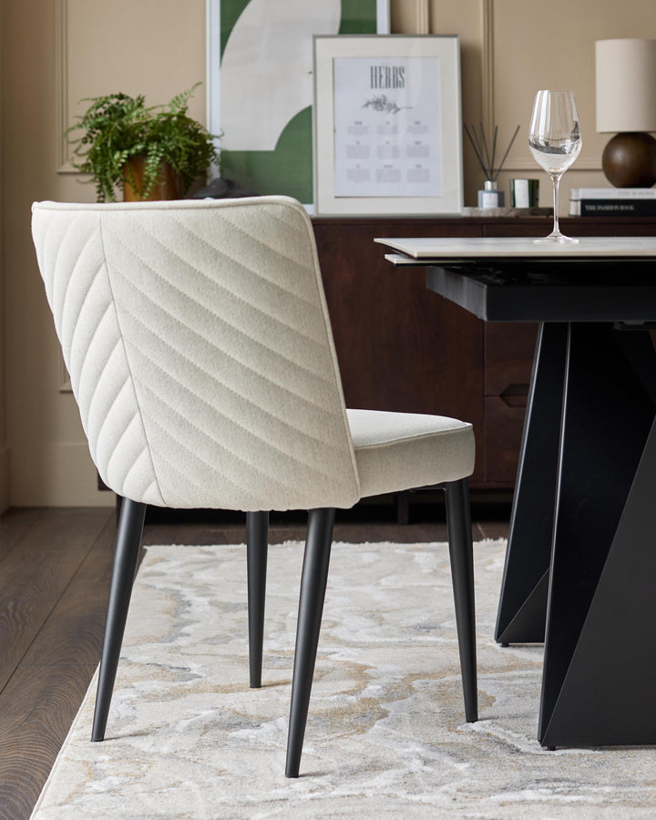 A dining space showcasing a cream quilted chair with black legs, paired with a modern black dining table and stylish sideboard.