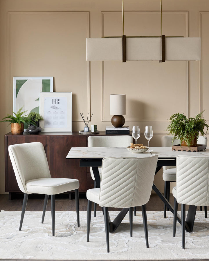 A stylish dining set featuring a marble table, upholstered chairs with black legs, and a modern linear light fixture.