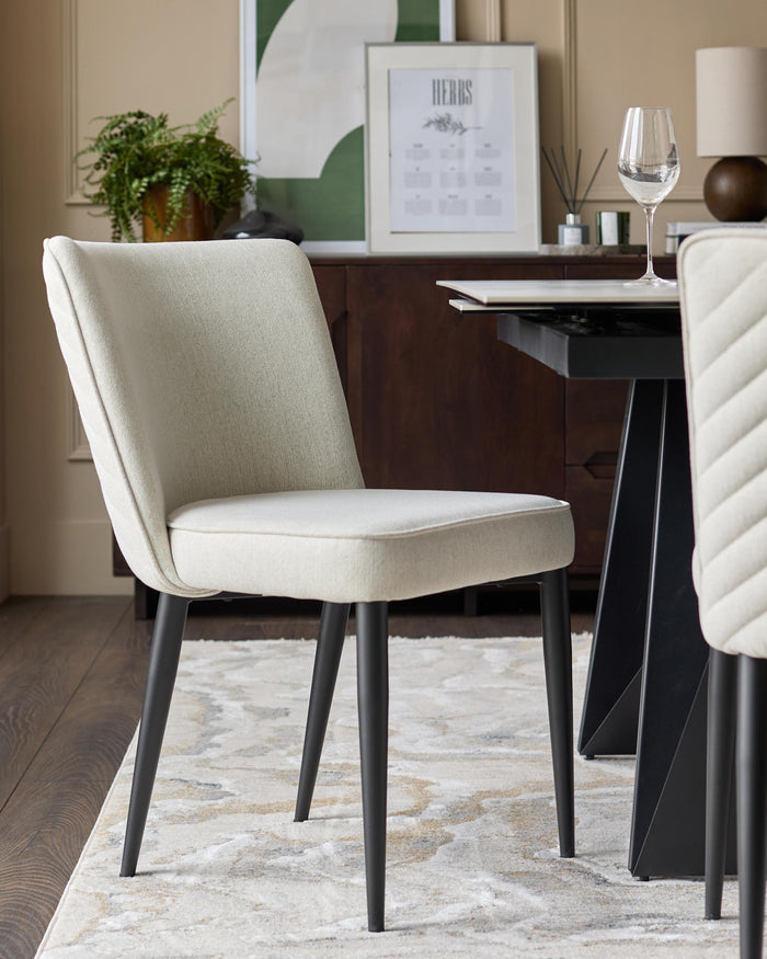 A modern dining room featuring a stylish chair with light upholstery and dark legs, set on a patterned rug next to a sleek table.