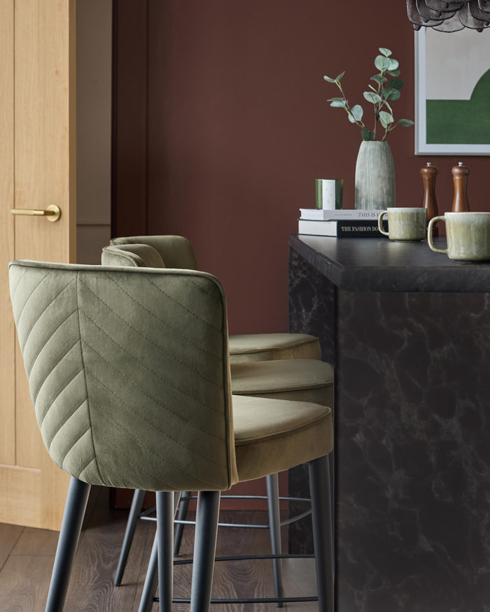Olive green bar stools with quilted design, paired with a dark marble kitchen island. Classic, stylish comfort.