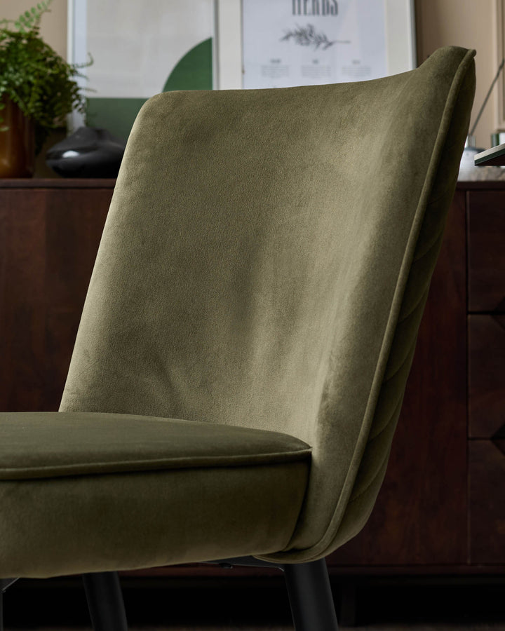 Close up of an olive green chair with black legs in front of a wooden cabinet and botanical print.