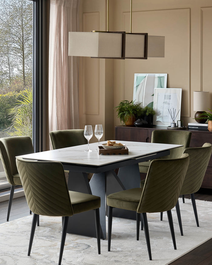 A modern dining set with six green velvet chairs, a marble table and a wooden sideboard, lit by a rectangular pendant light.