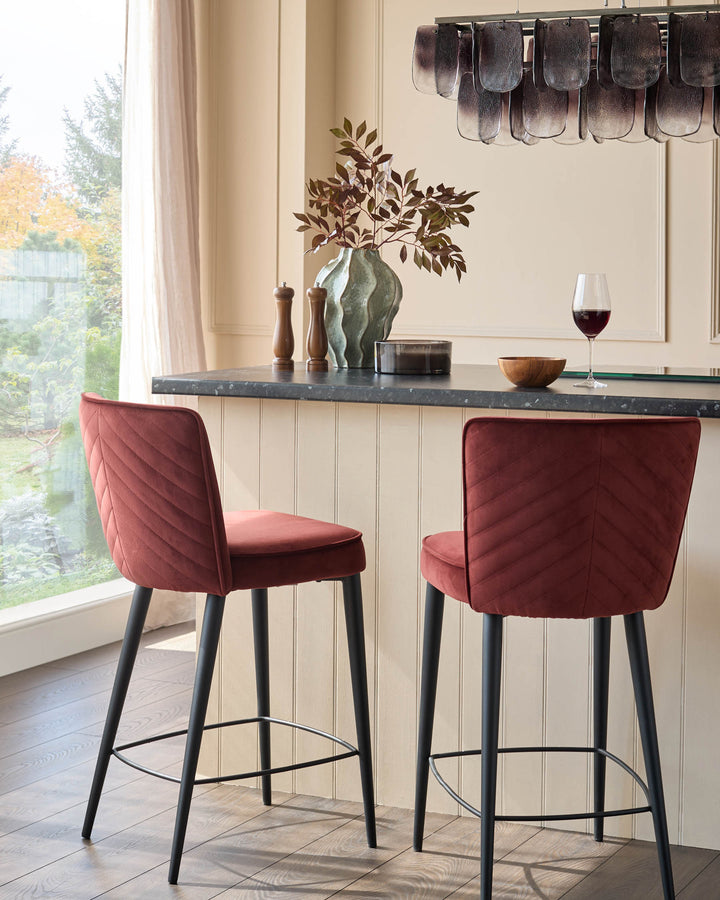 Two red velvet bar stools with black legs sit at a kitchen island, blending comfort and style.