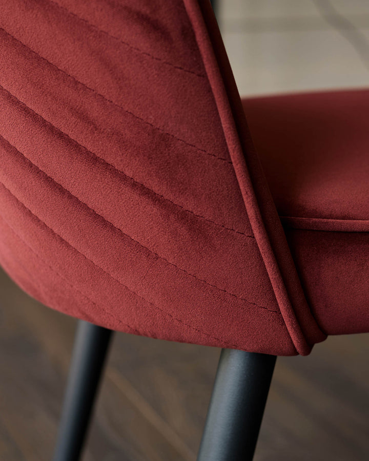 Close-up of a stylish, quilted, wine-red upholstered chair with black legs, showcasing its luxurious fabric and modern design.