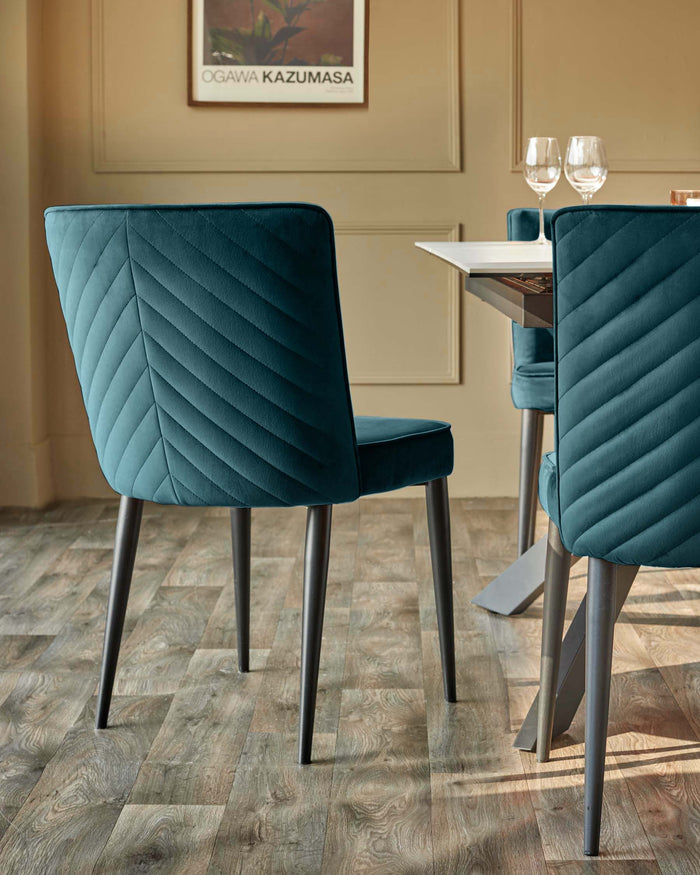 Teal velvet dining chairs with chevron stitching detail around a modern table. Stylish, contemporary dining room furniture.