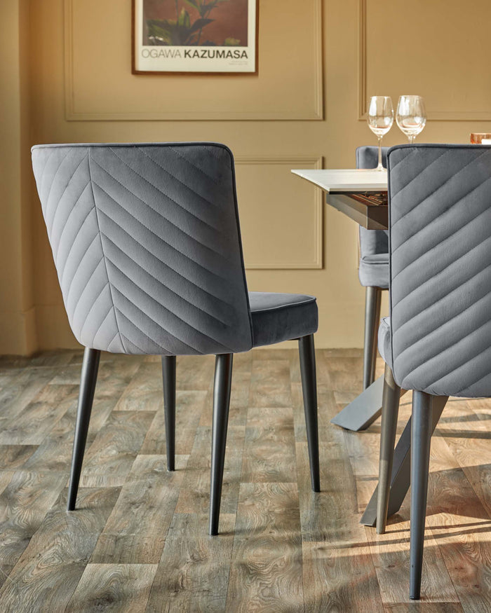 Grey velvet dining chairs sit at a table with wine glasses. Contemporary design for a stylish dining room.