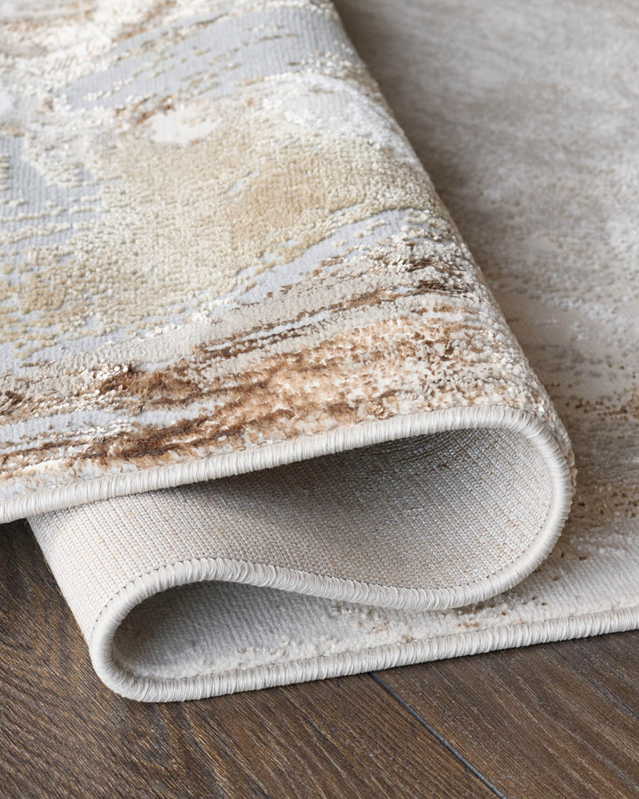 Close-up of a rolled, patterned rug showing the textured surface and backing on a wooden floor. Neutral colour palette.
