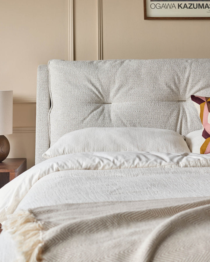 A stylish neutral bedroom with a textured headboard, white bedding, and a cosy fringed throw.