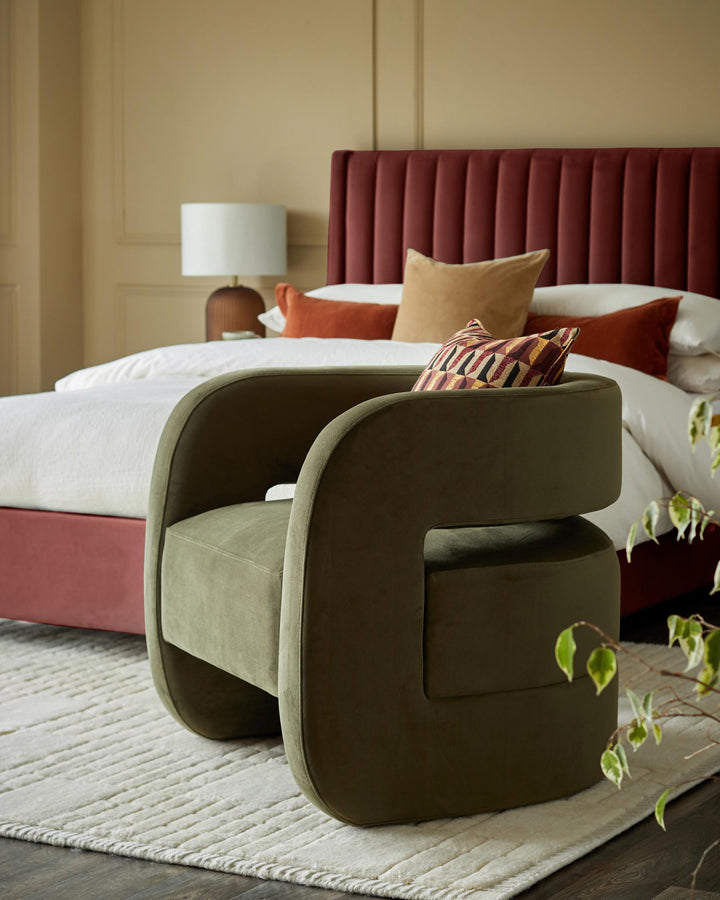 A cosy olive green armchair sits on a textured rug, with a luxurious bed visible in the background.