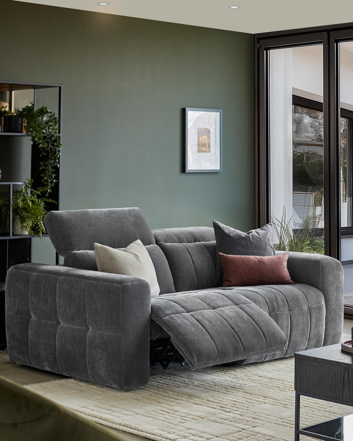 Stylish grey modular sofa with cushions and a recliner, set against a lush, modern backdrop. Perfect for a relaxing living room.
