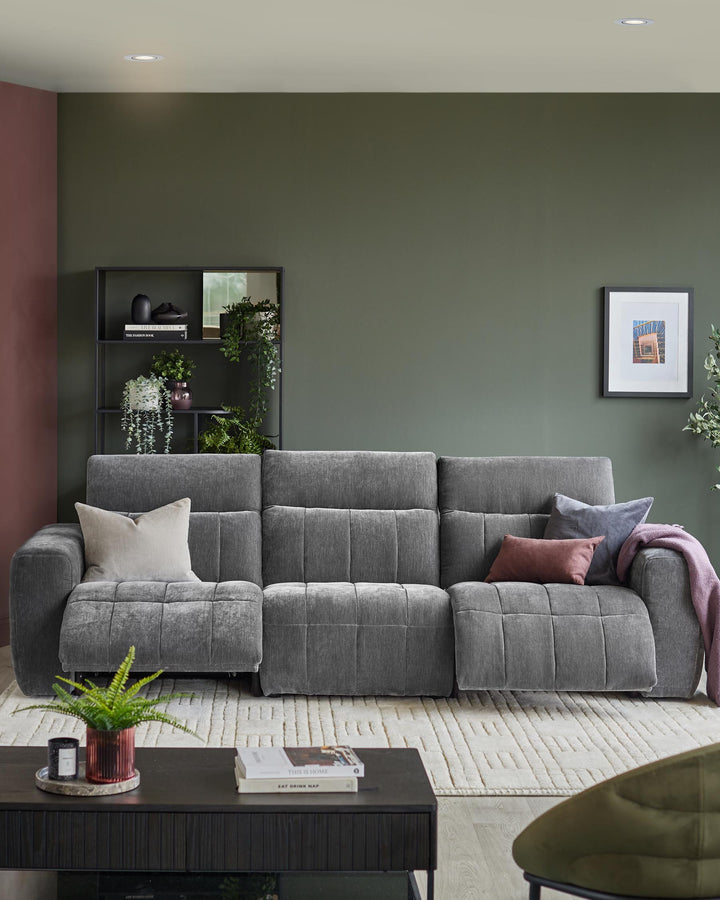 A grey three-seater sofa with reclining features, styled with cushions and throws, on a cream patterned rug.
