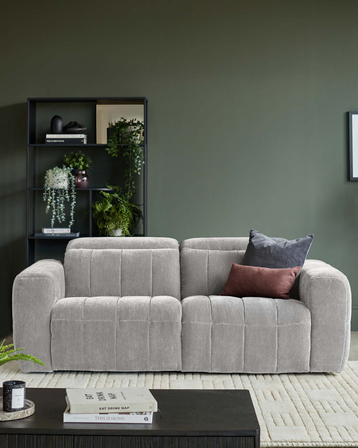 A modern grey sofa with cushions, paired with a dark wood coffee table and shelf unit against an olive green wall.