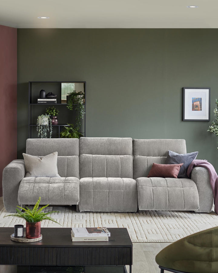A modern living room featuring a grey sofa, dark wood coffee table and a black shelving unit with plants and ornaments.
