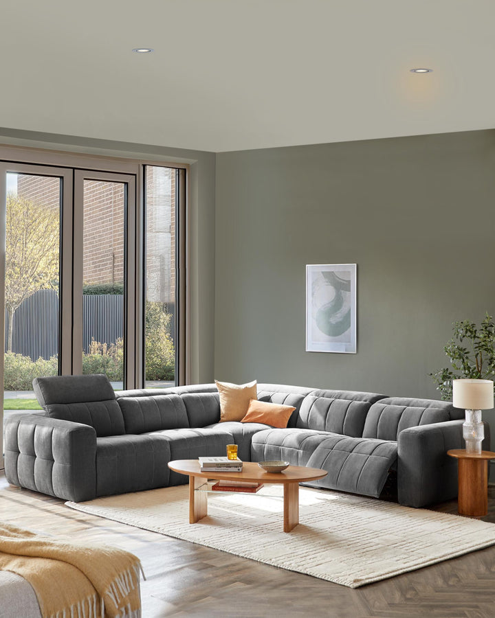 Modern gray sectional sofa with tufted design, wooden coffee table, decorative pillows, and a stylish lamp on a rug.