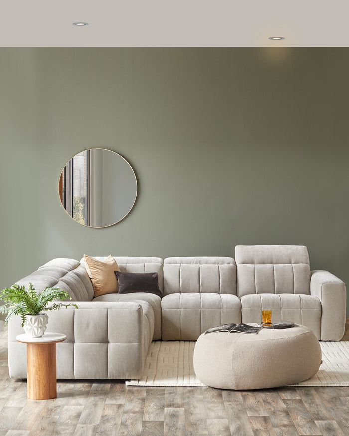 Elegant gray sectional sofa with textured upholstery, round mirror, chic side table, and a soft, rounded ottoman.