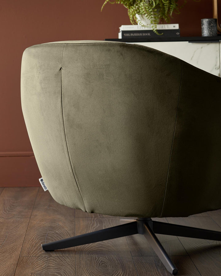Olive green swivel chair with a black base on a wooden floor. Books and plant are visible in the background.