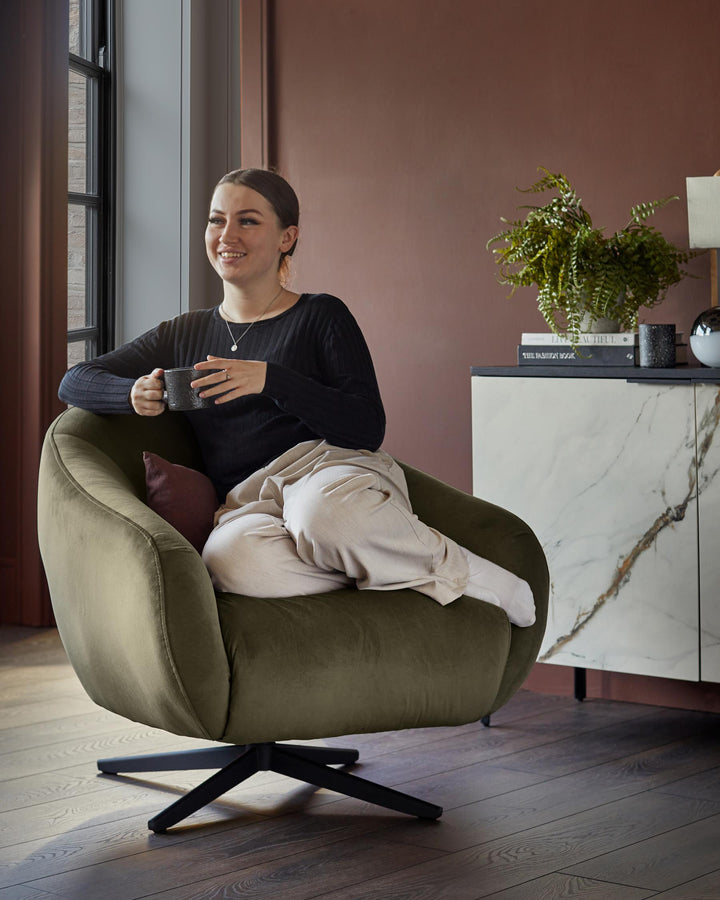 Olive swivel chair with a marble-effect sideboard, books, lamp and fern in a stylish living room with dark wood flooring.