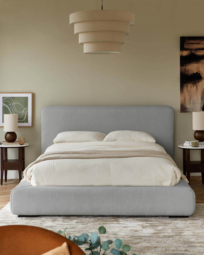 A light-grey upholstered bed sits centrally, with bedside tables either side, beneath a tiered ceiling light.