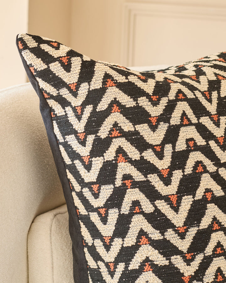 Black and cream geometric patterned cushion with rust orange accents, displayed on a neutral upholstered chair.